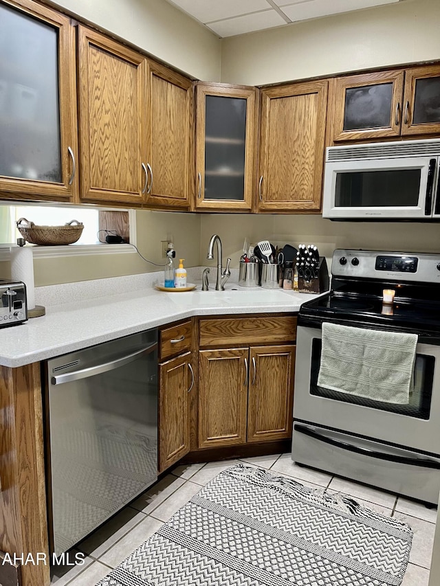 kitchen featuring light tile patterned floors, brown cabinetry, appliances with stainless steel finishes, and light countertops