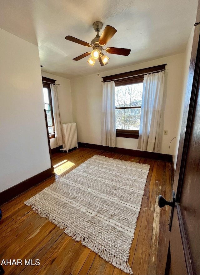 unfurnished bedroom featuring baseboards, multiple windows, radiator, and hardwood / wood-style flooring