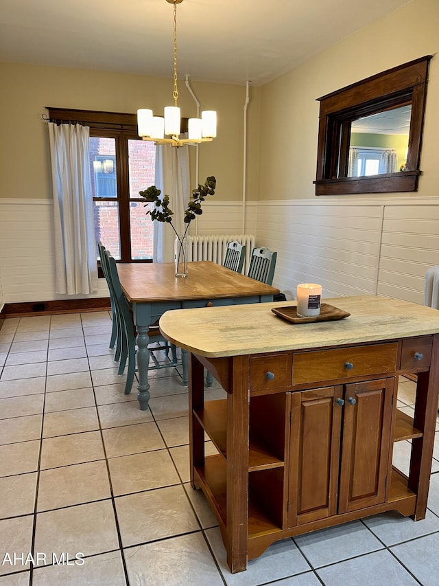 dining area with an inviting chandelier, radiator, light tile patterned floors, and wainscoting