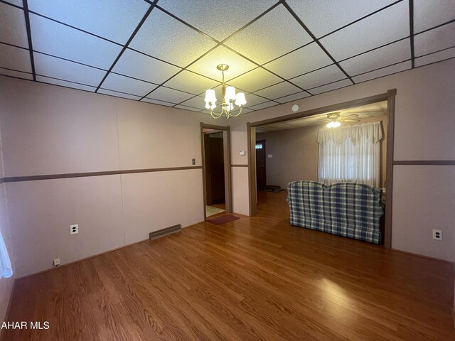empty room with a chandelier, a drop ceiling, wood finished floors, and visible vents