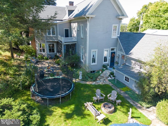 rear view of property featuring a yard, a trampoline, and a fire pit