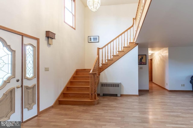 foyer with radiator, a high ceiling, light hardwood / wood-style flooring, and a notable chandelier