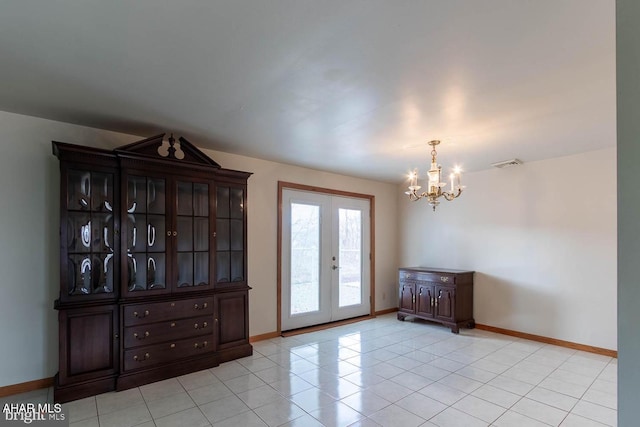 empty room with light tile patterned floors, a notable chandelier, and french doors