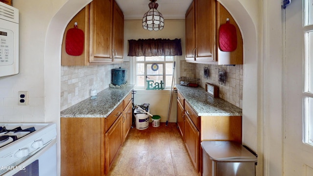 kitchen featuring light stone countertops, light wood-type flooring, backsplash, white appliances, and hanging light fixtures