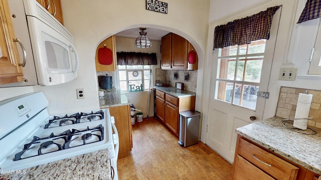 kitchen with light stone countertops, light wood-type flooring, white appliances, and backsplash