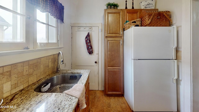 kitchen featuring decorative backsplash, white refrigerator, light stone counters, and sink