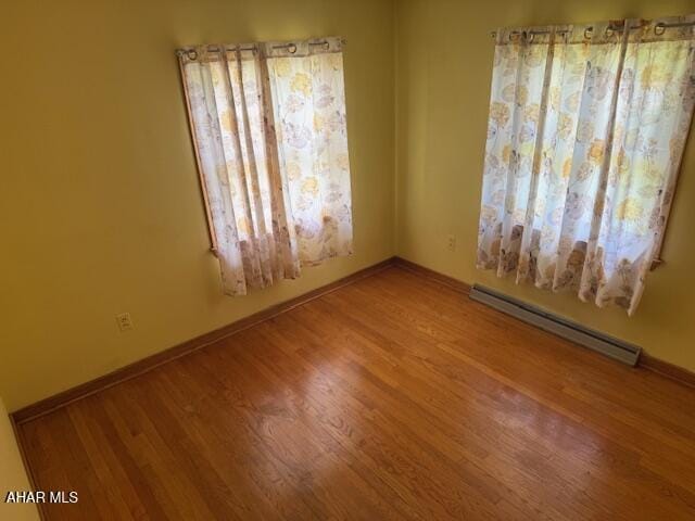 empty room with a baseboard heating unit, wood finished floors, and baseboards