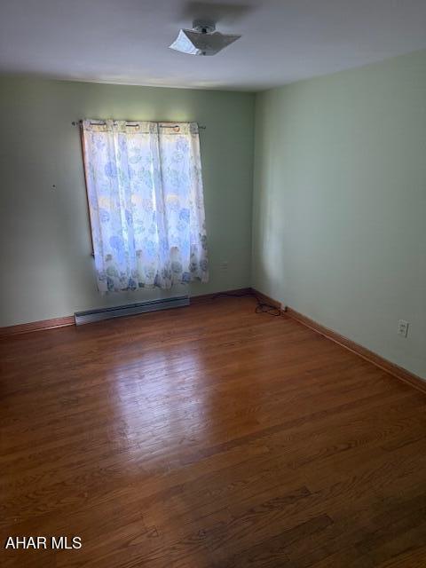 spare room featuring a baseboard radiator, wood finished floors, and baseboards