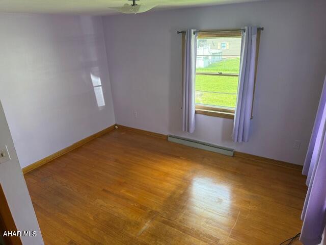 spare room featuring a baseboard heating unit, light wood-type flooring, baseboards, and ceiling fan