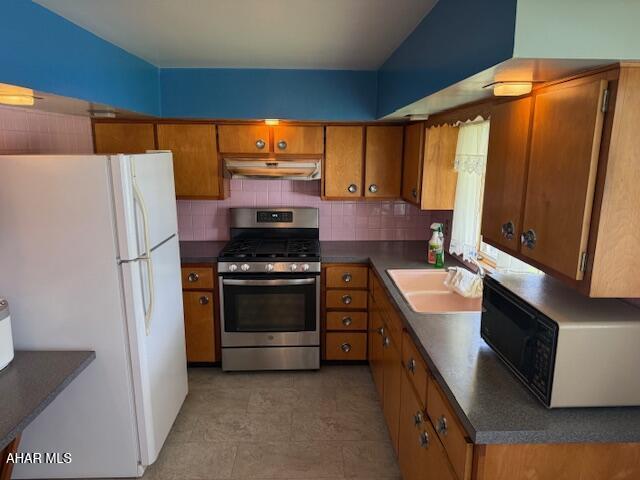 kitchen featuring gas stove, freestanding refrigerator, black microwave, under cabinet range hood, and brown cabinetry