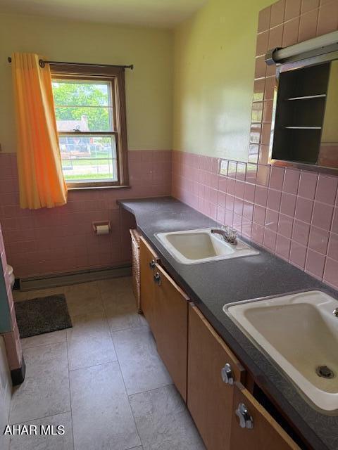 kitchen with a sink, tile walls, dark countertops, light tile patterned flooring, and wainscoting