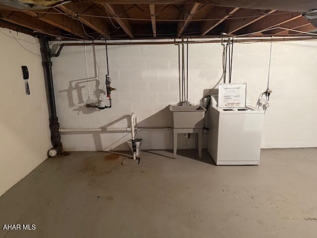 unfinished below grade area with concrete block wall, washing machine and clothes dryer, and a sink