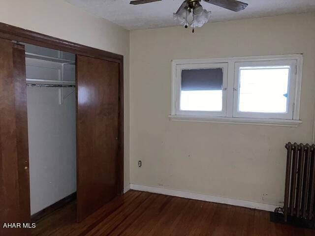 unfurnished bedroom featuring a closet, radiator, dark wood-type flooring, and ceiling fan