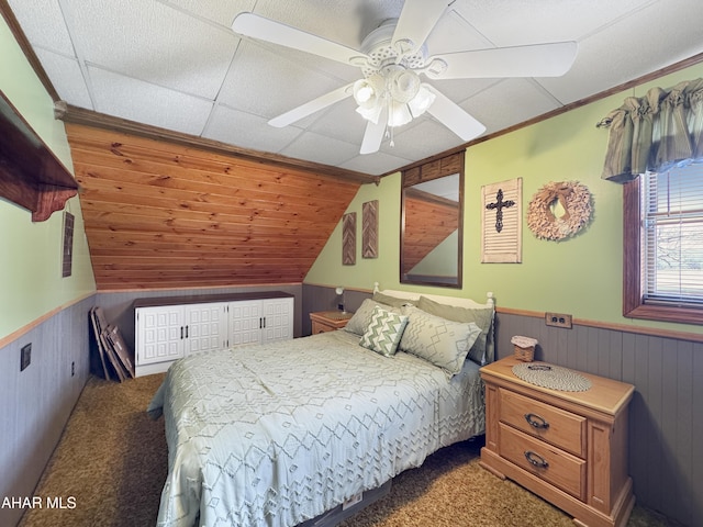 bedroom featuring a ceiling fan, wainscoting, vaulted ceiling, wood walls, and dark carpet