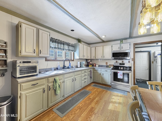 kitchen with light wood finished floors, light countertops, appliances with stainless steel finishes, a sink, and a textured ceiling