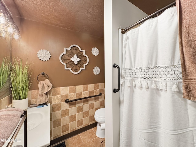 full bath with toilet, tile patterned floors, a textured ceiling, vanity, and tile walls