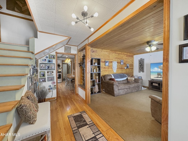 living room with light wood-style flooring, wooden walls, ceiling fan with notable chandelier, stairway, and crown molding