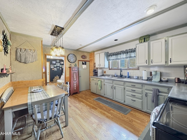 kitchen with electric stove, light wood-style flooring, a textured ceiling, pendant lighting, and a sink