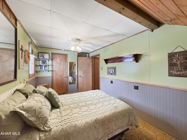 bedroom with a ceiling fan, wainscoting, wood walls, and carpet flooring