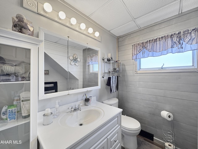 bathroom with toilet, a paneled ceiling, wood walls, and vanity