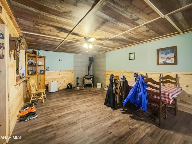 interior space with ceiling fan, wood-type flooring, wooden ceiling, a wood stove, and wood walls