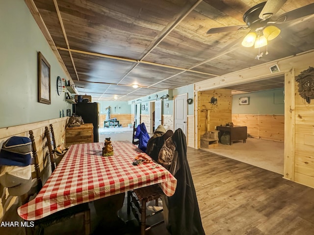 dining room with hardwood / wood-style floors, ceiling fan, and wood walls