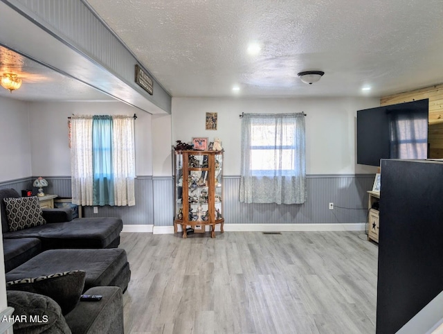 living room featuring wooden walls, light hardwood / wood-style floors, and a textured ceiling