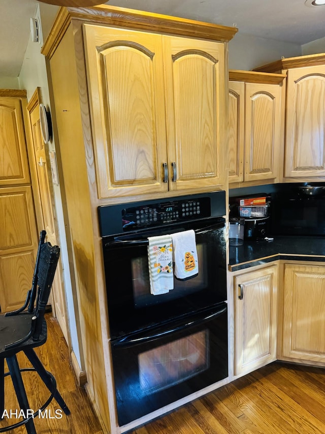 kitchen with light brown cabinetry, black double oven, and hardwood / wood-style floors