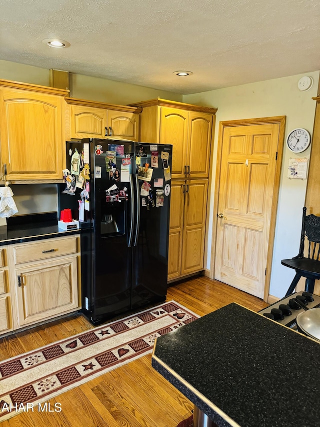 kitchen with a textured ceiling, light hardwood / wood-style floors, and black fridge