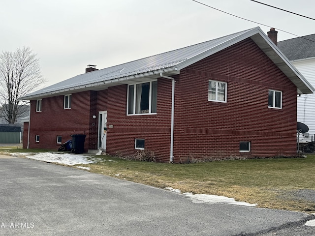 view of side of home featuring brick siding, metal roof, a chimney, and a lawn