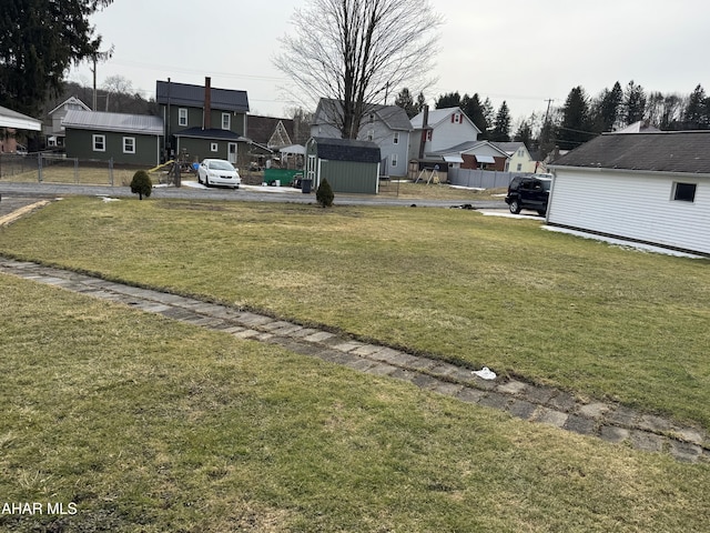 view of yard featuring an outbuilding, fence, a residential view, and a storage unit