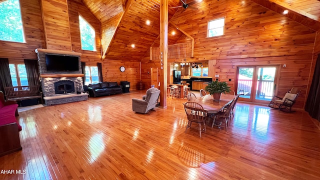 living room with wood ceiling, wooden walls, a stone fireplace, and high vaulted ceiling