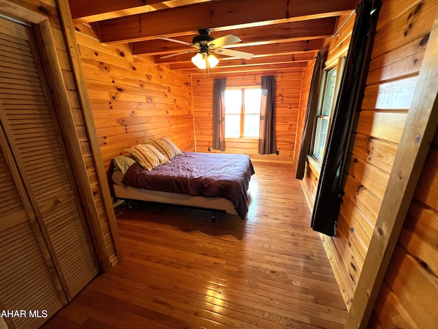 bedroom featuring beamed ceiling, ceiling fan, wooden walls, and light hardwood / wood-style floors