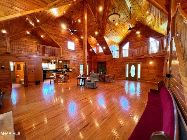 living room with high vaulted ceiling, wooden walls, wooden ceiling, and ceiling fan