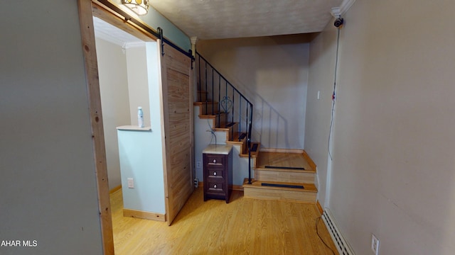 stairway with wood-type flooring, a textured ceiling, a baseboard radiator, ornamental molding, and a barn door