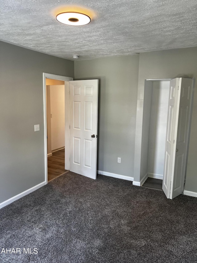 unfurnished bedroom with a closet, dark carpet, and a textured ceiling