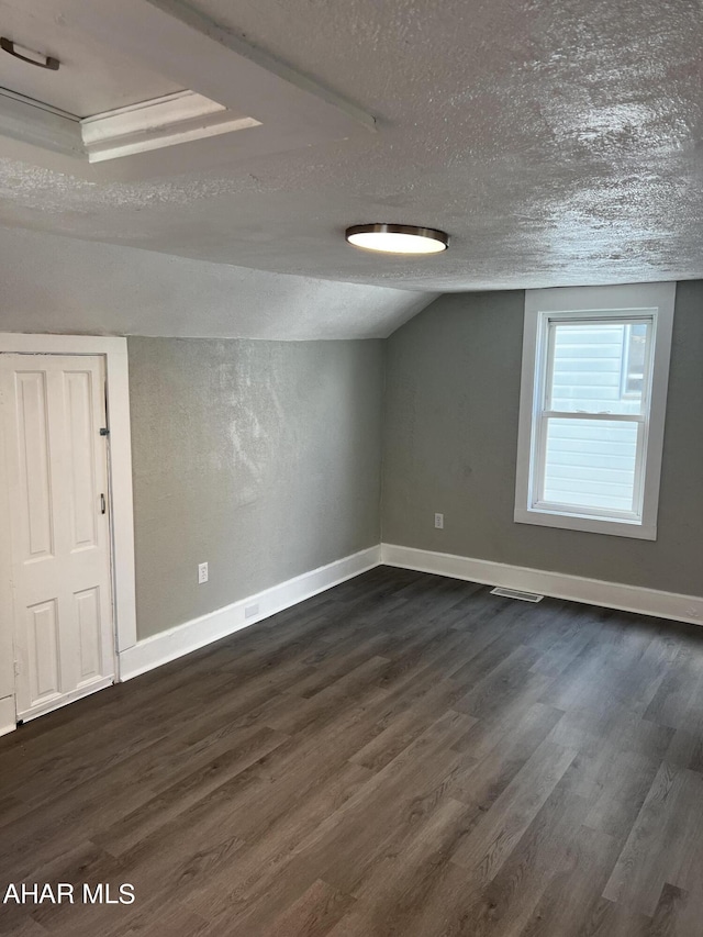 additional living space with dark hardwood / wood-style flooring, lofted ceiling, and a textured ceiling