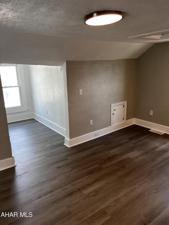 spare room with dark hardwood / wood-style flooring, lofted ceiling, and a textured ceiling