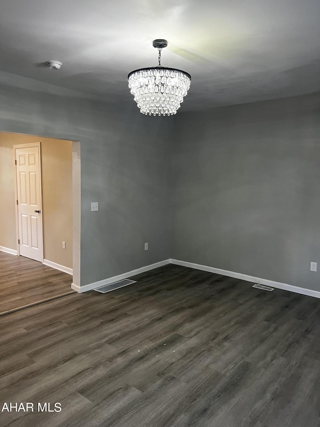 unfurnished room featuring an inviting chandelier and dark wood-type flooring