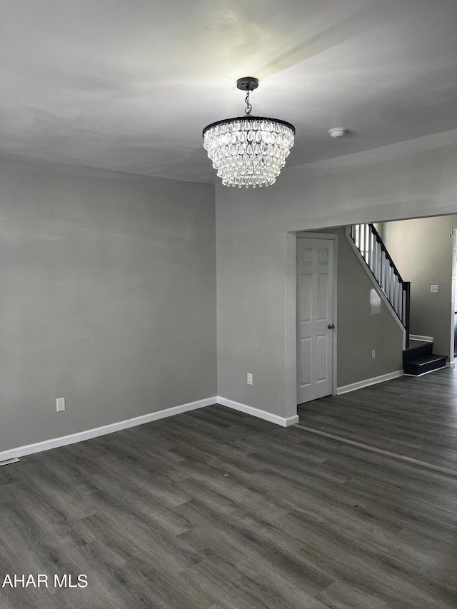 unfurnished room featuring an inviting chandelier and dark wood-type flooring