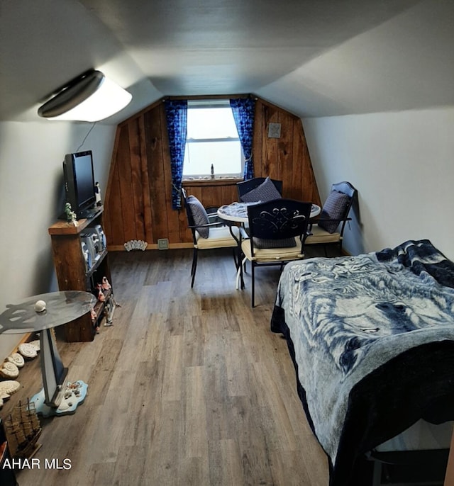 bedroom with wood walls, light wood-type flooring, sink, and vaulted ceiling