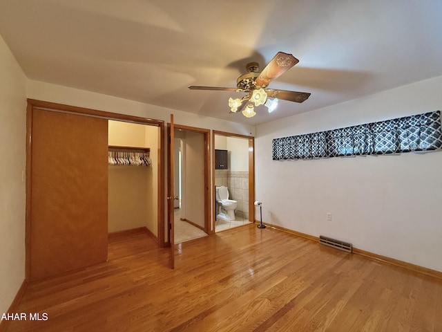 unfurnished bedroom featuring ceiling fan, ensuite bathroom, a closet, and hardwood / wood-style flooring