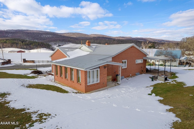 snow covered back of property featuring a mountain view and a carport