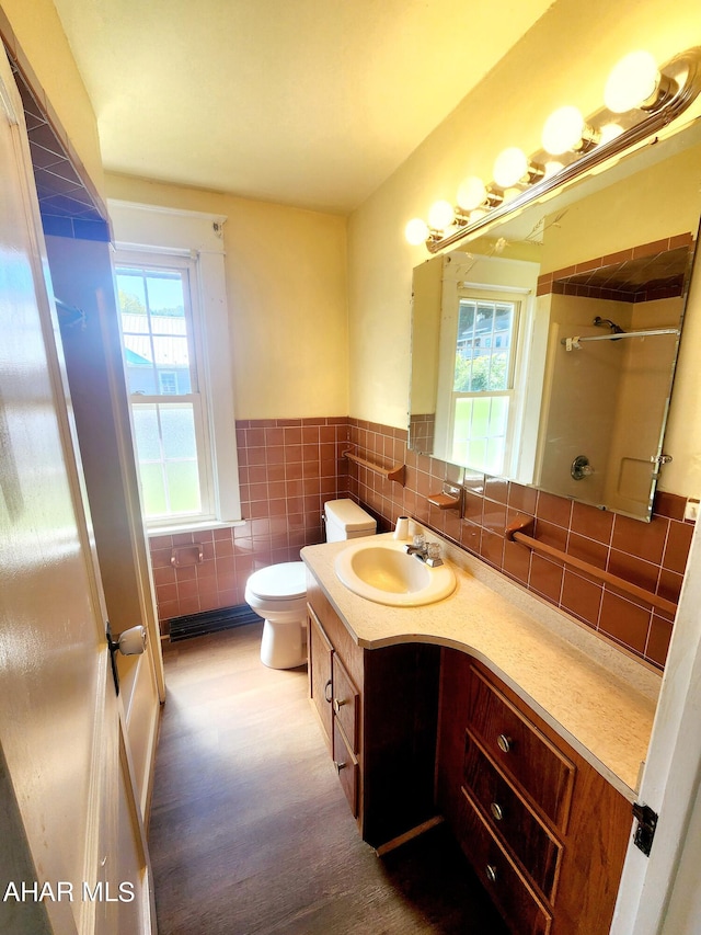 bathroom with vanity, toilet, tile walls, and a tile shower