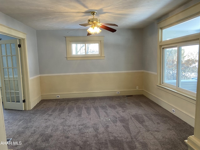 unfurnished room with ceiling fan and dark colored carpet