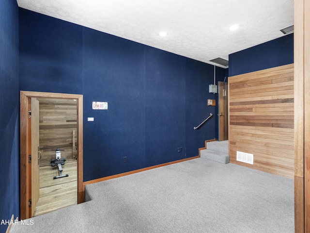 spare room featuring wooden walls, carpet floors, and a textured ceiling