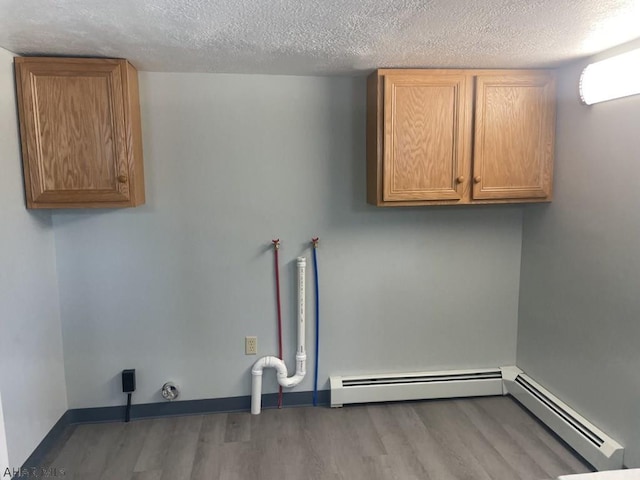 laundry area featuring cabinets, wood-type flooring, a textured ceiling, and baseboard heating