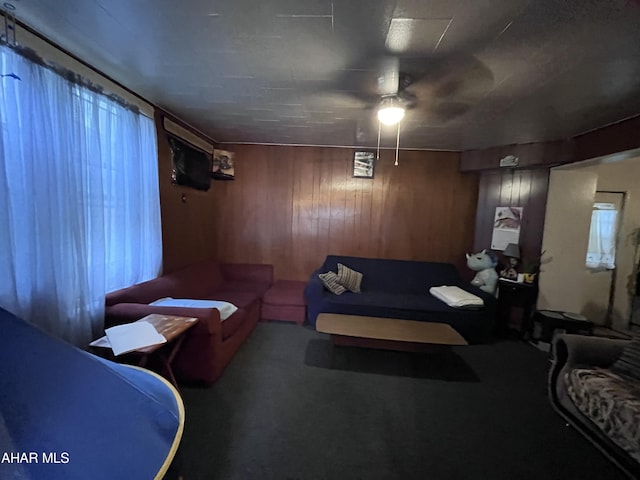 carpeted living room featuring ceiling fan and wood walls