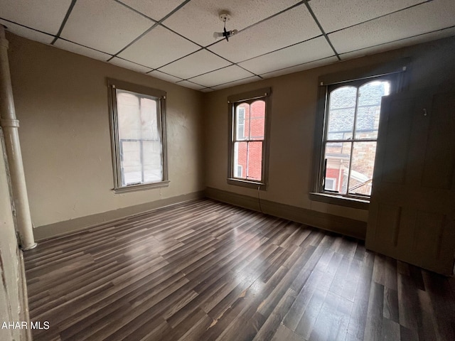 unfurnished room with a paneled ceiling, a healthy amount of sunlight, and dark wood-type flooring