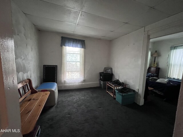 interior space with a paneled ceiling and dark carpet